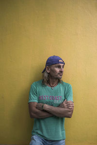 Young man looking away while standing against yellow wall