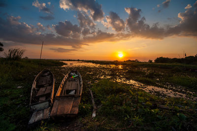 Abandoned boat on field against sky during sunset