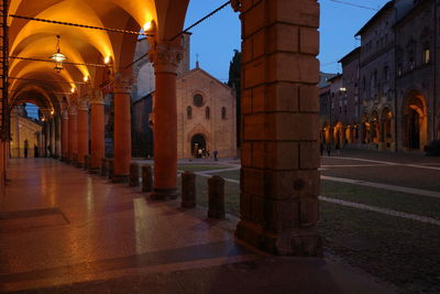 Illuminated street amidst buildings against sky at night