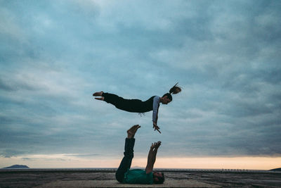 Full length of man balancing woman against cloudy sky