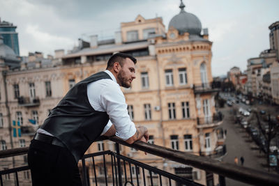 Man standing on railing against buildings in city