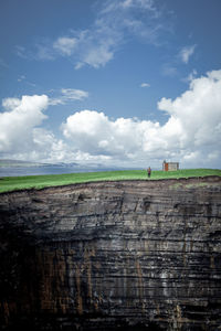Woman standing on cliff against cloudy sky