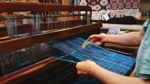 Midsection of woman weaving looms with shuttle at workshop
