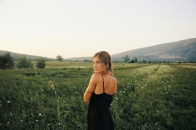 Portrait of young woman standing on field against clear sky