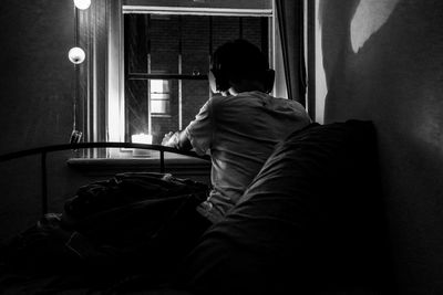 Rear view of man listening music while looking through window