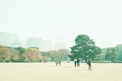 People in park against buildings in city against clear sky