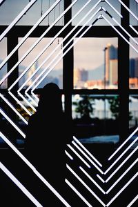 Silhouette woman standing by window against sky
