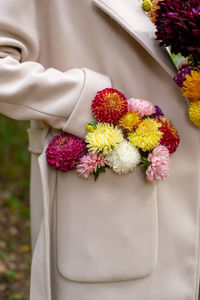 Women's hands in the pocket of a beige coat with a bouquet of autumn flowers