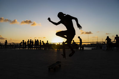 Silhouette people jumping on beach against sky during sunset