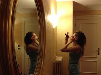 Reflection of woman on mirror doing make-up in illuminated room
