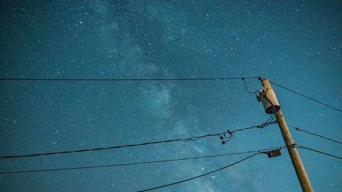 Low angle view of electricity pylon against star field in sky