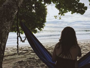 Rear view of woman sitting on hammock at beach