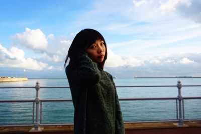 Beautiful young woman standing in front of sea against sky