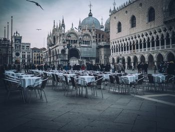 Chairs and tables at sidewalk cafe against buildings and sky in city