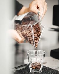 Close-up of hand pouring beans in glass on grinder