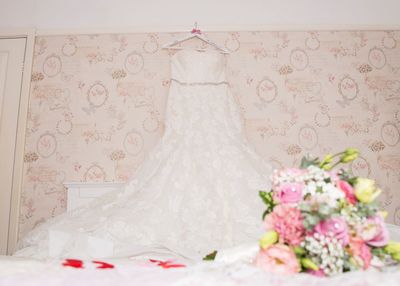 Low angle view of wedding dress hanging on bed against wall