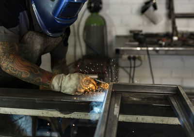 Unrecognizable male welder using welding machine on metal detail while working at workbench in factory