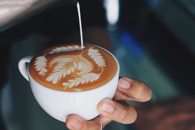 Cropped image of man pouring milk on coffee cup