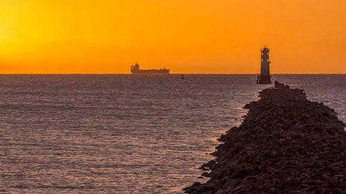 Lighthouse by sea against sky during sunset