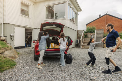 Mother and daughter loading stuff with father and girl having fun near house