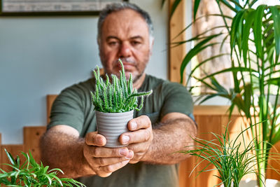 Mature bearded man holding a pot with cactus. taking care of home flowers and succulents. 