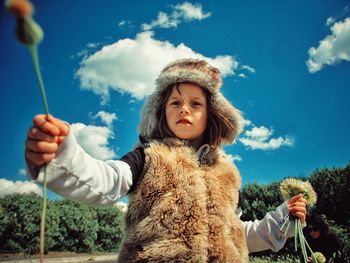 Portrait of girl with dandelions against sky