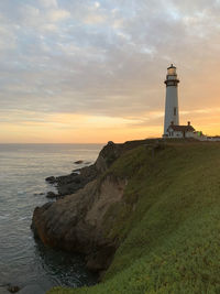 Lighthouse by sea against sky during sunset