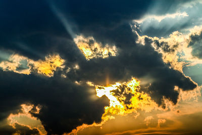 Low angle view of sunlight streaming through clouds