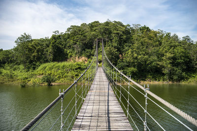 Rear view of woman walking on footbridge against sky