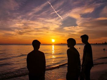 Silhouette people on beach against sky during sunset