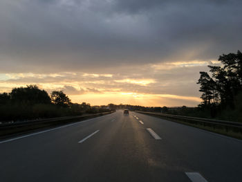 Country road along trees and against cloudy sky