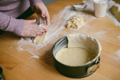 Midsection of woman preparing dough at table in kitchen