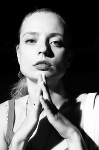 Portrait of beautiful woman with hands clasped against black background