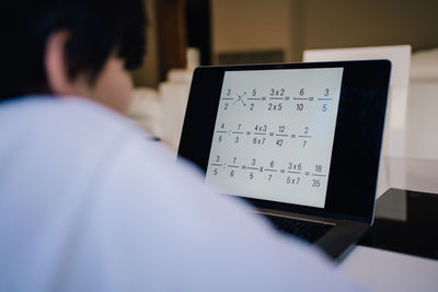 Rear view kid looking at laptop, child with notebook, close up of boy learning mathematics formulas.