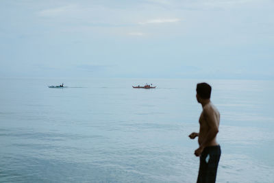 Rear view of man standing in sea against sky