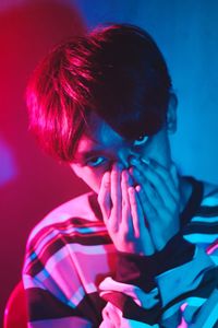 Close-up portrait of young man covering mouth at night