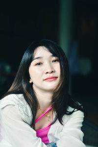 Portrait of young woman standing against black background