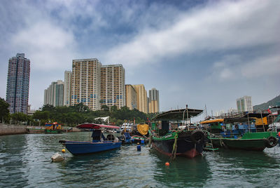 Boats moored on river by buildings in city against sky