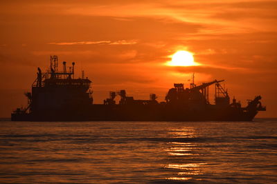 Silhouette ship in sea against orange sky