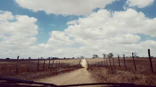 Road passing through field against cloudy sky