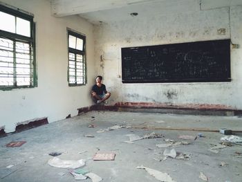 Full length of young man levitating against wall in abandoned classroom