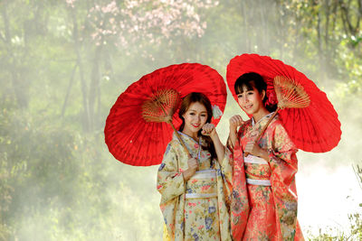 Portrait of smiling young woman holding red umbrella against trees