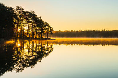 The still lake reflects the beauty of nature as dawn breaks in a peaceful idyllic swedish landscape.