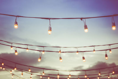 Low angle view of illuminated light bulbs hanging against sky