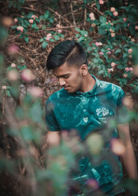 Young man looking down while standing amidst plants in forest