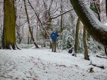 Man standing by bare trees in forest during winter