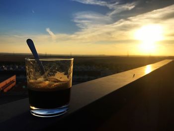 Close-up of drink on table at beach against sky during sunset
