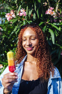 Smiling young woman with ice cream standing in front of plant