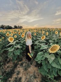 Woman standing on sunflower field against sky