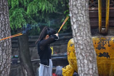 Woman with incenses praying against tree trunk